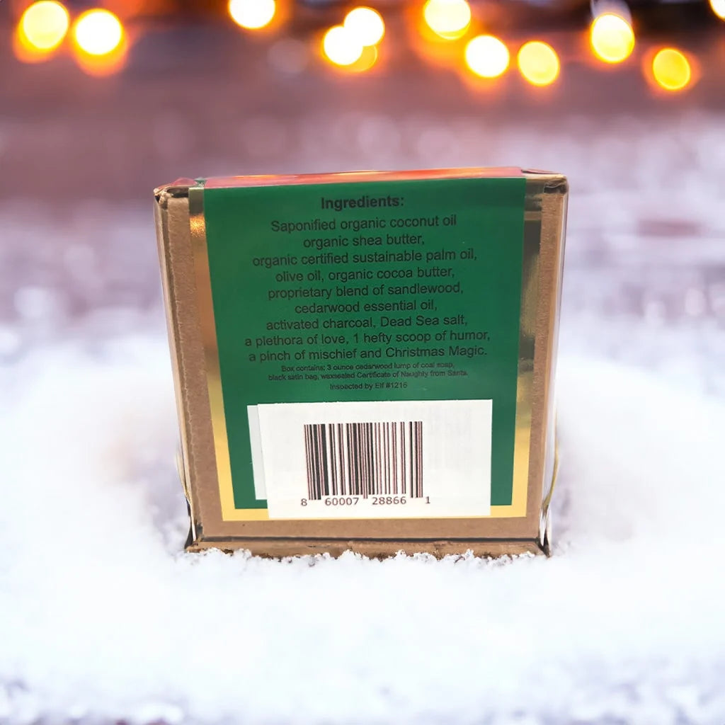 Lump of Coal cardboard box with a green backside label with a barcode labeling the ingredients sitting on top of a pile of snow with a background of blurred Christmas lights