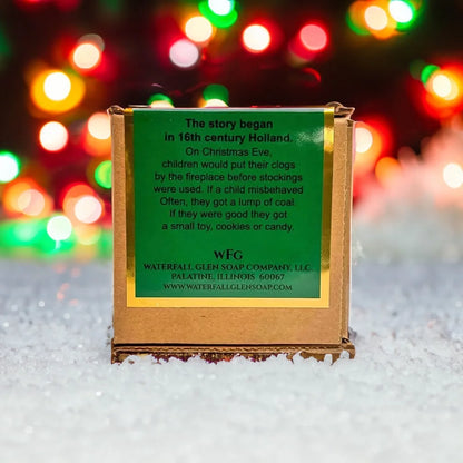Lump of Coal cardboard box with a green backside label sitting on top of a pile of snow with a background of blurred Christmas lights