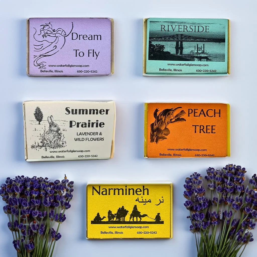 Five floral scented bar soaps on top of a light blue background above two bundles of lavender